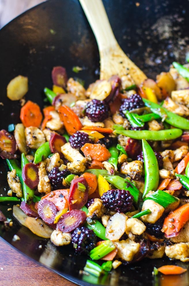 A wooden spoon stirring stir fry in a wok.