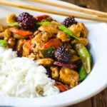 A white bowl filled with half white rice and half stir fry. Chopsticks rest on the bowl.