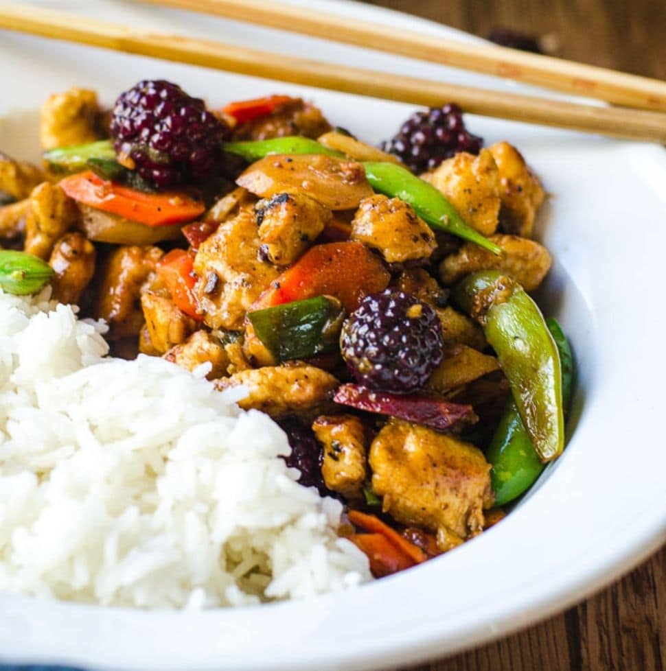 A white bowl filled with half white rice and half stir fry. Chopsticks rest on the bowl.