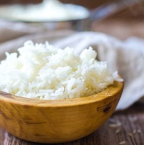 Closeup of a wooden bowl filled with white rice in front of a pot of cooked rice.