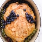 A whole roasted chicken garnished with blueberries and rosemary in a dutch oven.