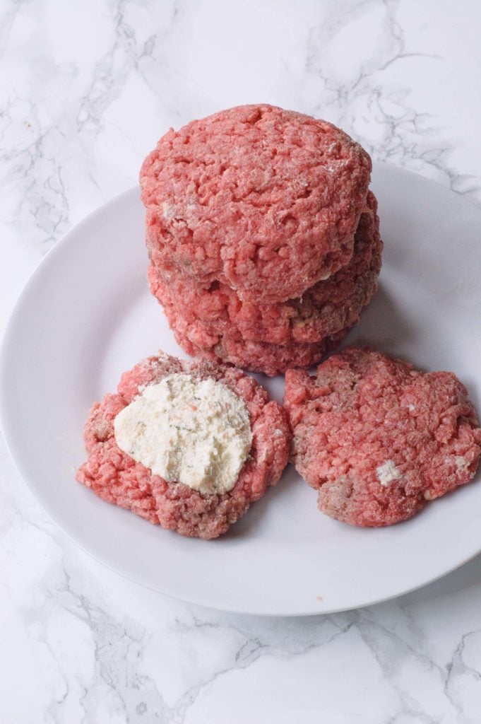 a white plate with three stuffed raw breakfast burgers and one being assembled