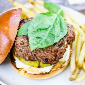 Two giant basil leaves rest on top of a garlic cheeseburger.