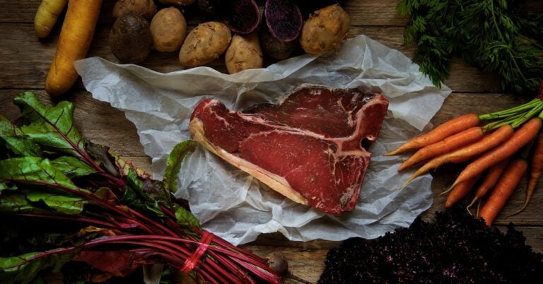 A steak on butcher paper surrounded by other ingredients for dinner.