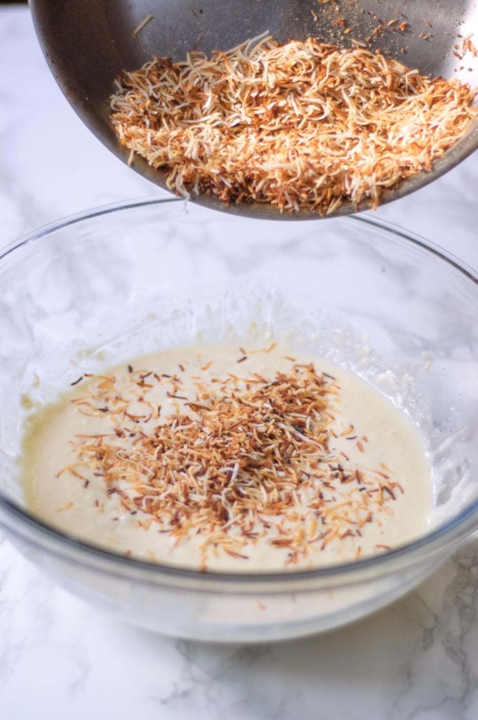 A pan of toasted coconut being poured into chocolate chip pancake batter