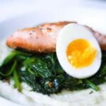 seared salmon and a medium boiled egg on wilted spinach and grits in a white bowl