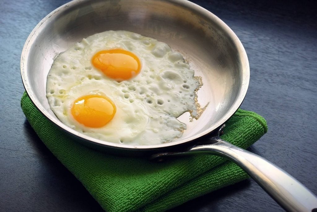 A stainless steel pan making fried eggs on a green towel