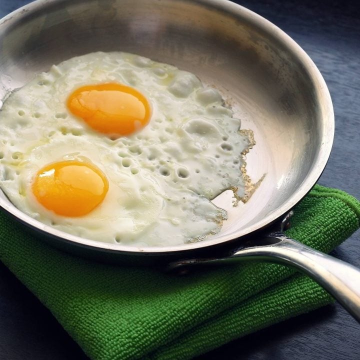 A stainless steel pan making fried eggs on a green towel