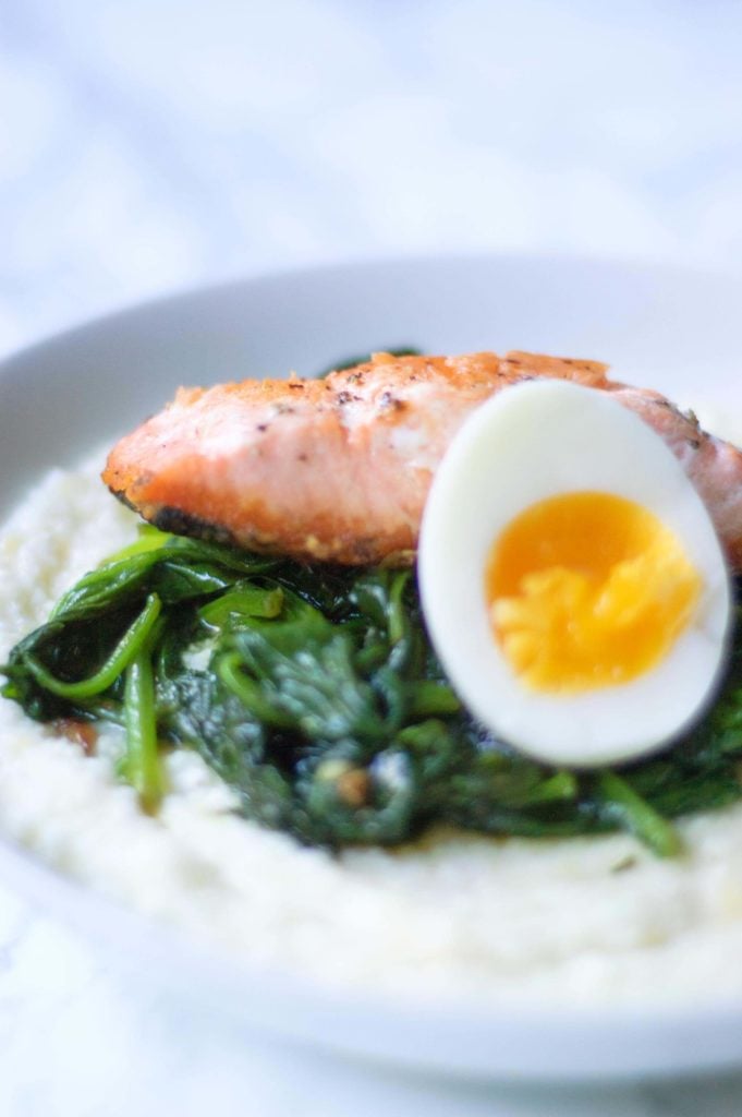 closeup image of half of a medium boiled egg next to wilted spinach and a salmon filet