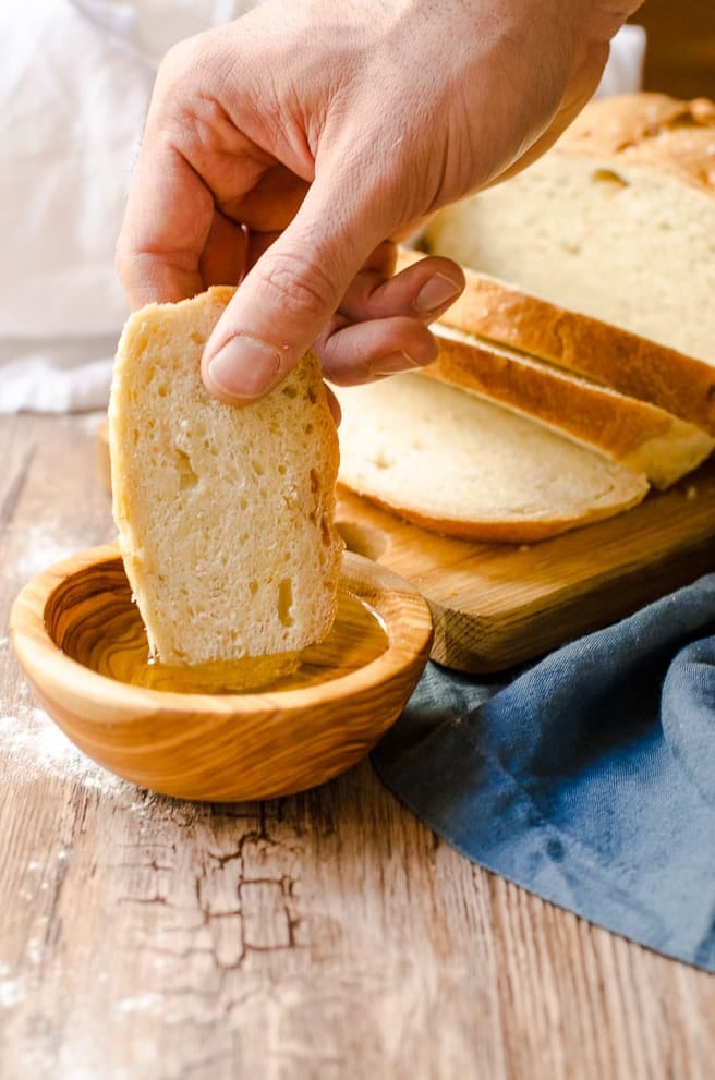 A hand dipping a slice of artisan bread into a bowl of olive oil