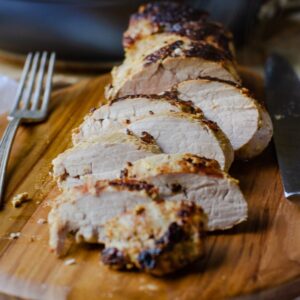 closeup image of sliced roasted pork tenderloin next to a fork on a wooden cutting board
