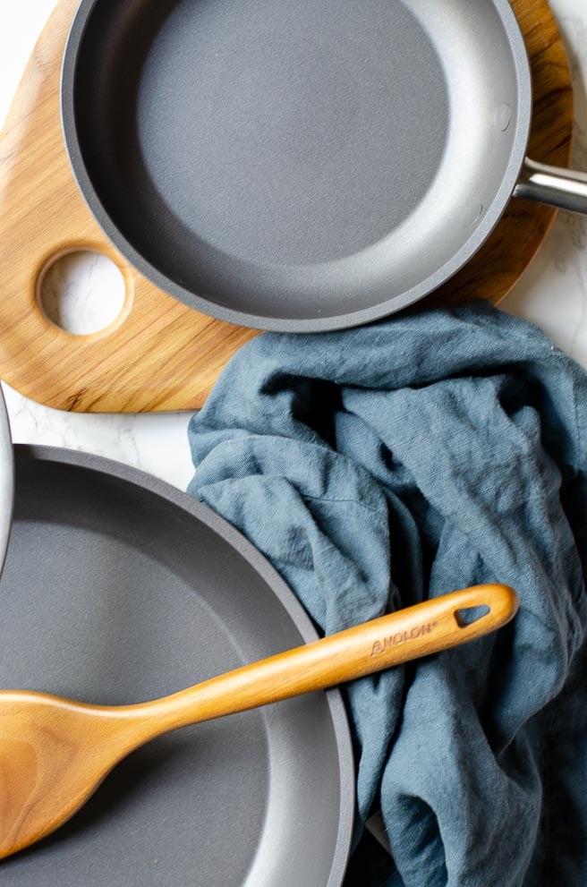 overhead shot of two nonstick frying pans with wooden utensils and a blue napkin