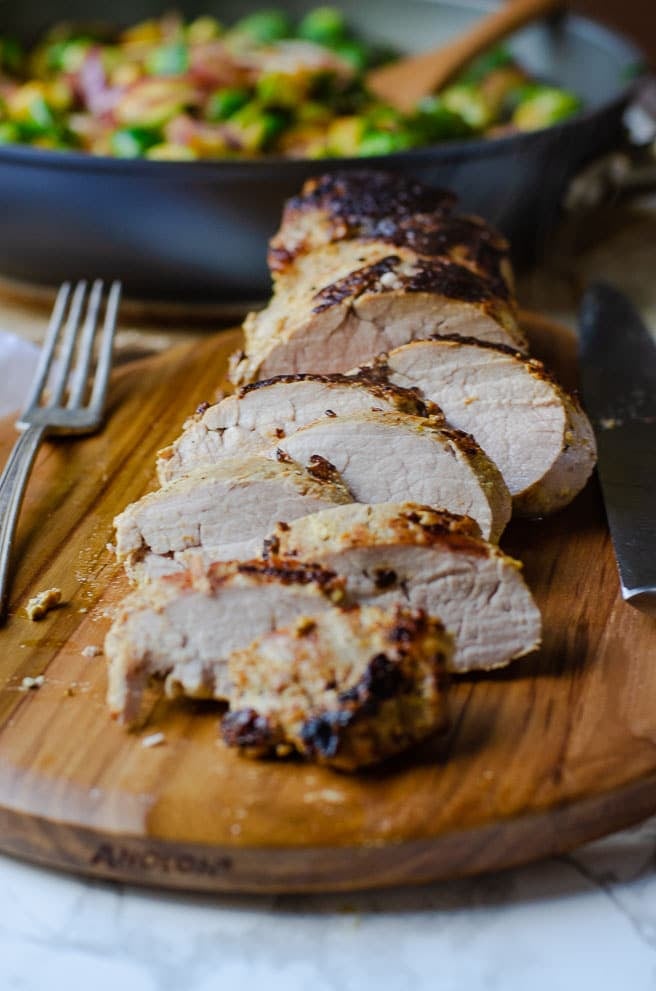 a closeup image of a sliced pork tenderloin on a wooden cutting board next to a fork