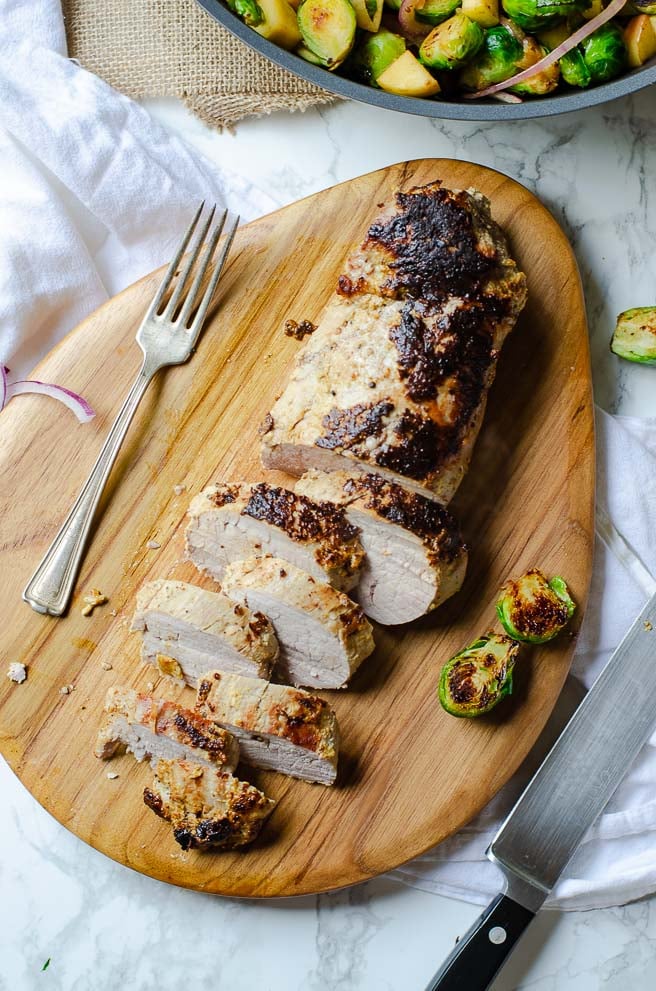 overhead shot of sliced roasted pork tenderloin on a wooden cutting board next to a fork
