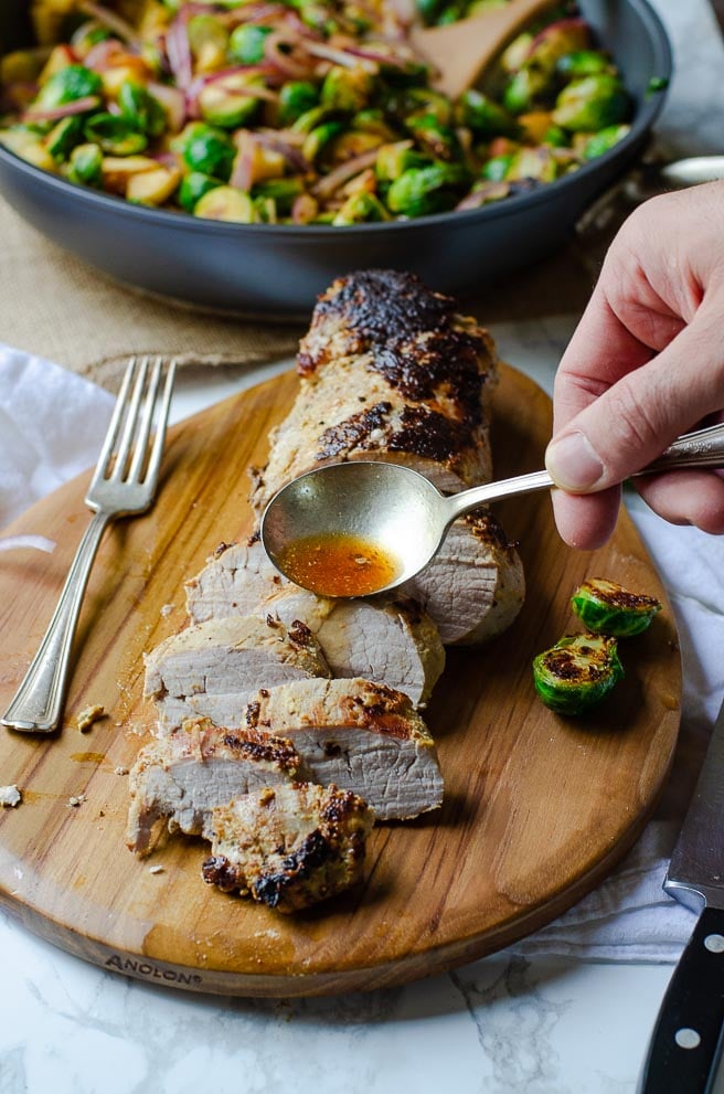 A spoonful of white wine mustard sauce being poured onto sliced roasted pork tenderloin