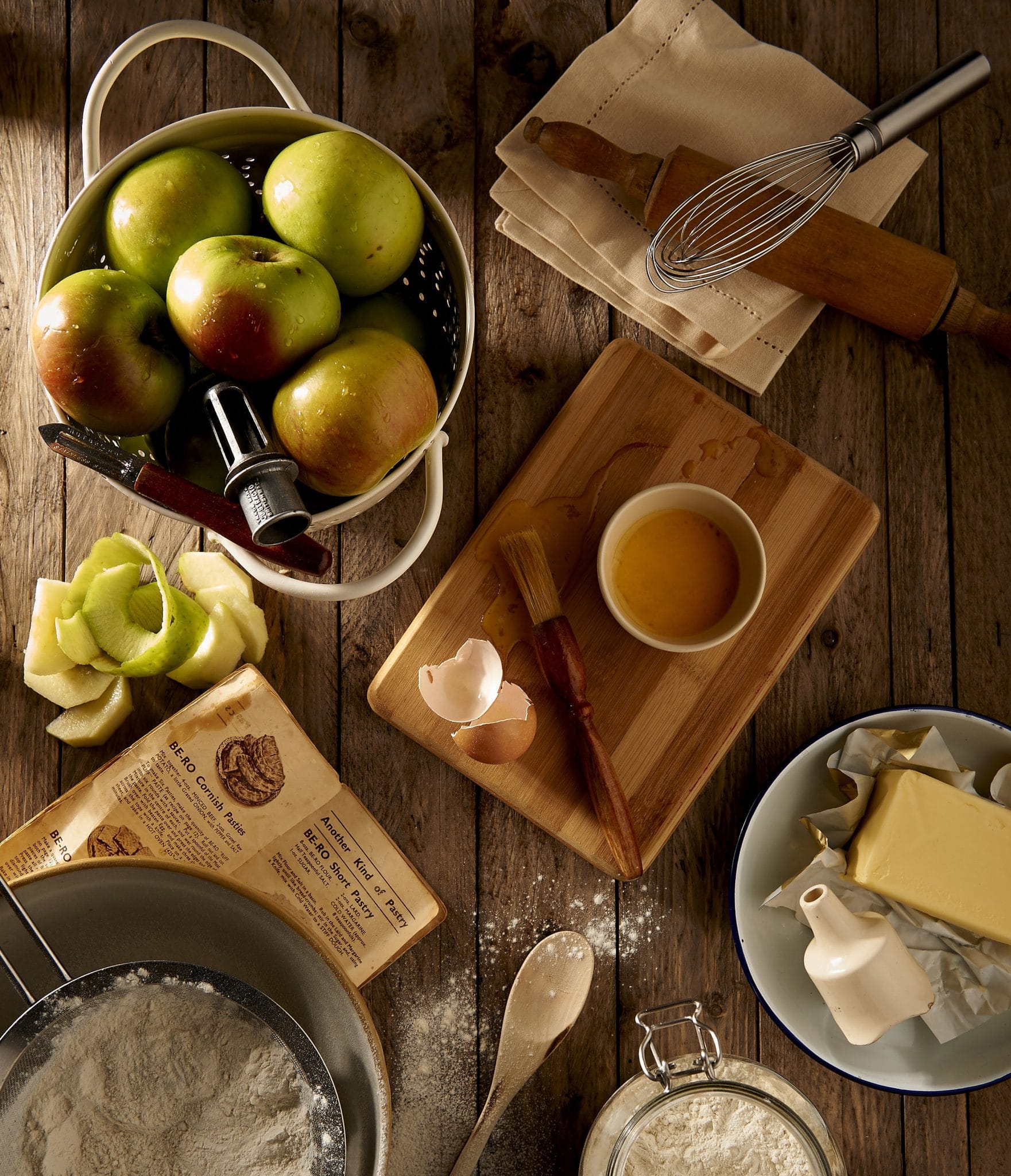 All the ingredients needed to make apple pie surrounding a wooden board.