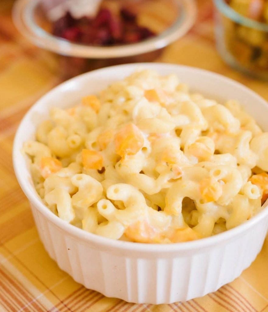 A white bowl of creamy mac and cheese sprinkled with chopped butternut squash