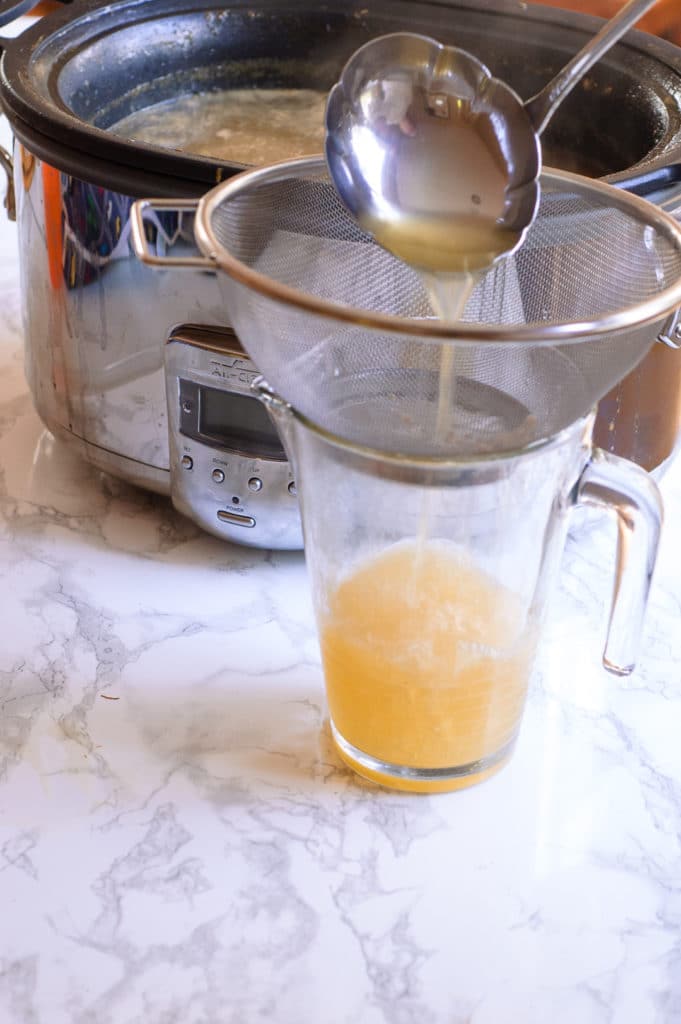 A ladle pouring turkey stock through a strainer and into a jar