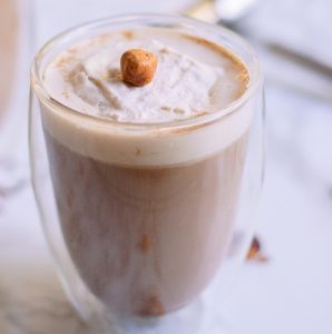 A single hazelnut sits on top of freshly whipped cream on a coffee cocktail.