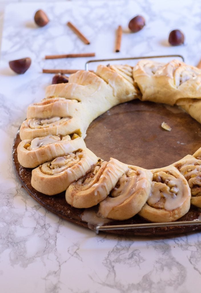 Icing dripping off of a chestnut roll wreath on a baking stone.