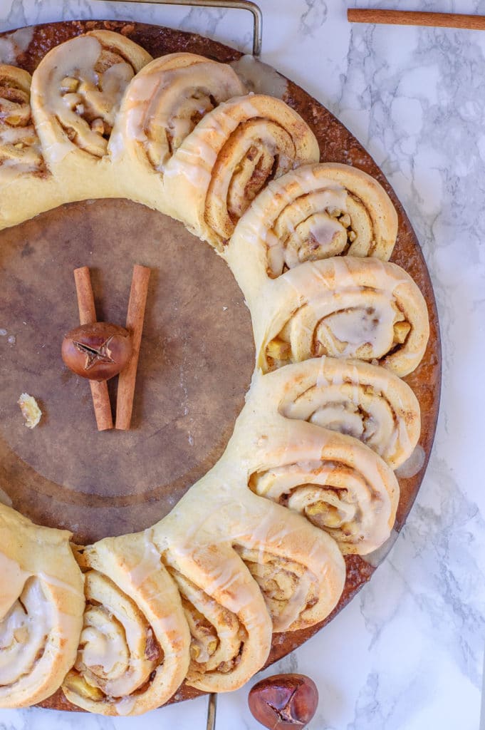 Overhead view of the chestnut roll wreath on a baking stone. It has two cinnamon sticks and a chestnut in the middle