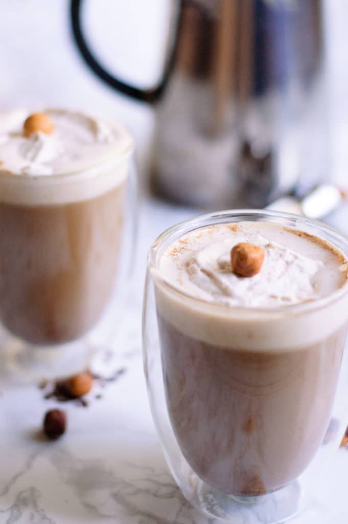 Two glasses of coffee cocktails garnished with shipped cream and hazelnuts.