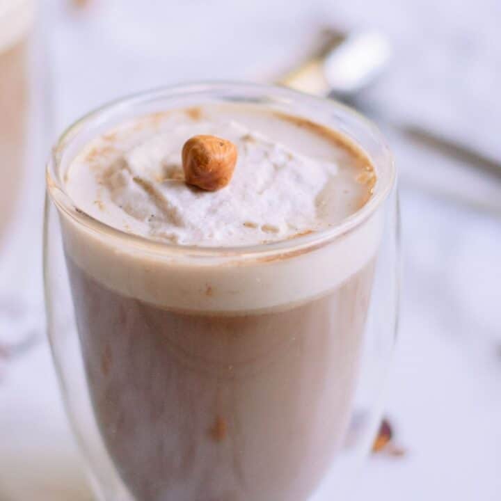 A clear cup filled with a brown liquid, with foam on top