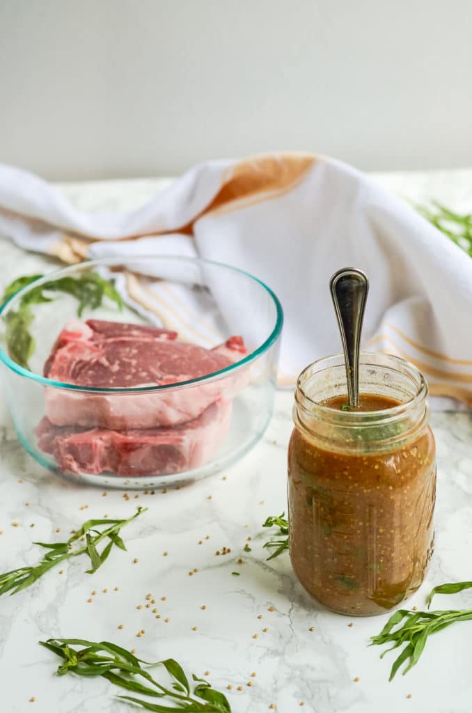 A bowl of pork chops behind a mustard marinade in a mason jar.