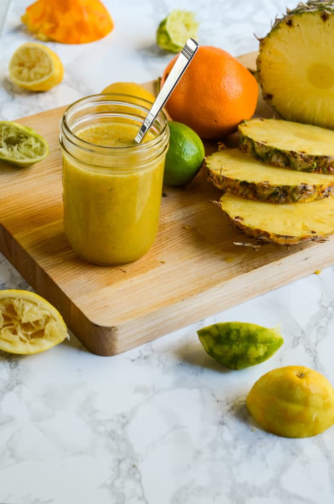 a mason jar of salmon marinade next to squeezed citrus and a cut pineapple