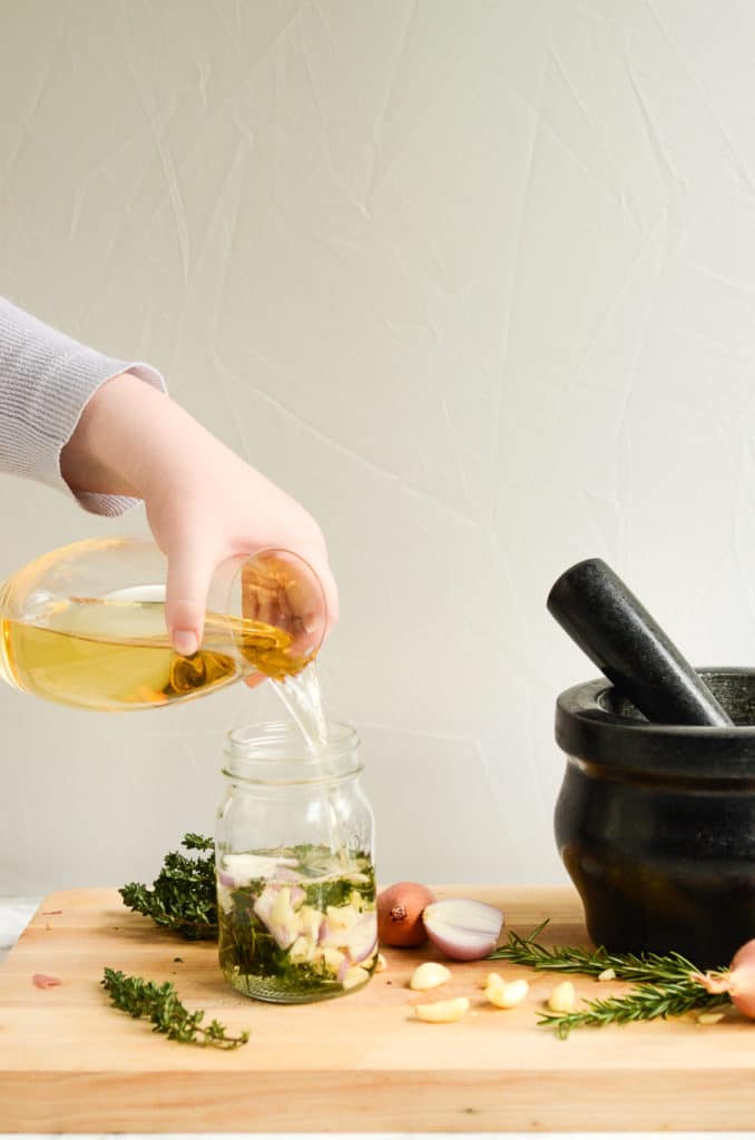A hand pouring white wine into a marinade for grilled veggies.