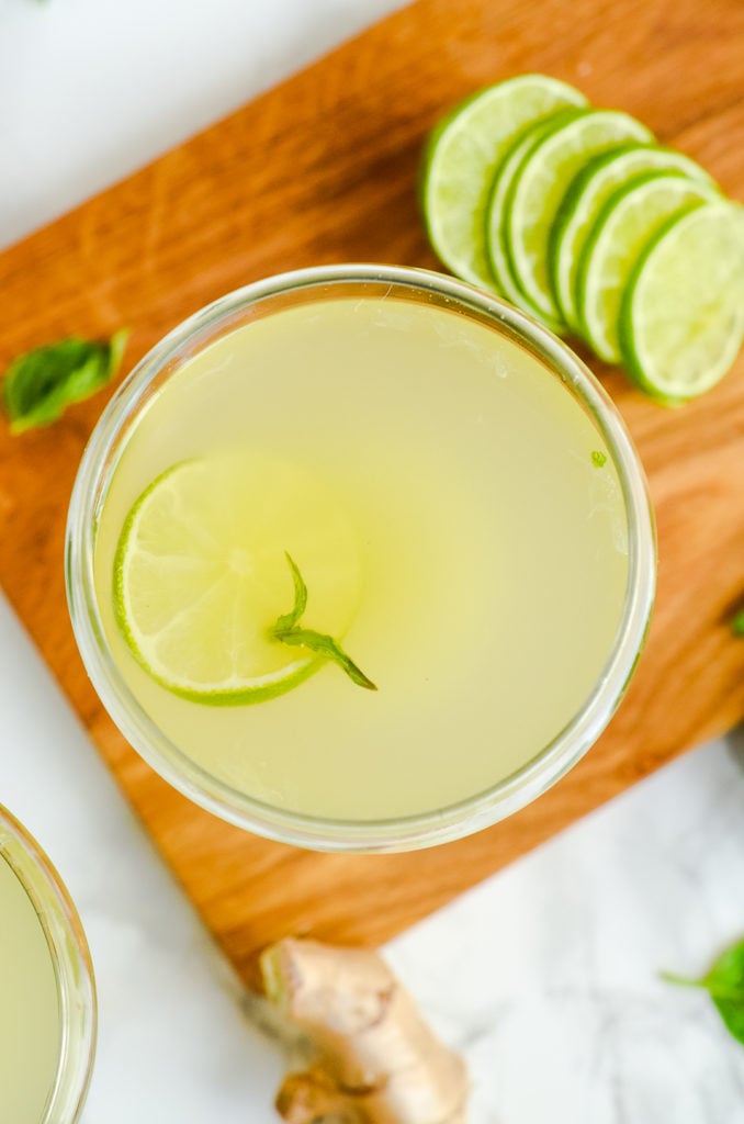 Overhead image of one basil ginger gimlet in a cocktail glass with limes and fresh basil