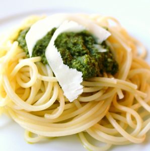 A pile of pesto and shaved parmesan on top of a plate of cooked spaghetti.