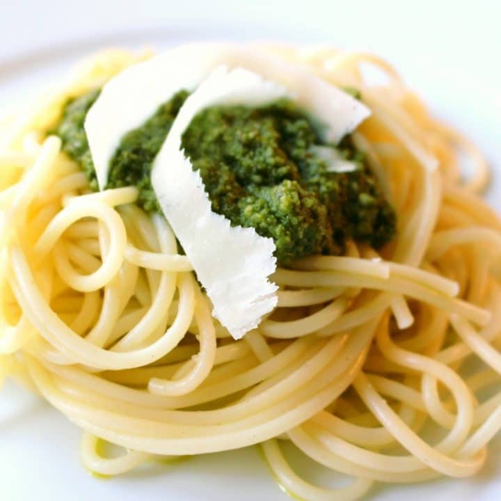 A pile of pesto and shaved parmesan on top of a plate of cooked spaghetti.