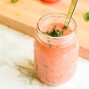 A mason jar of tomato basil marinade next to a cutting board of ingredients.