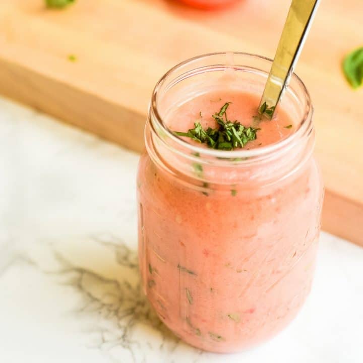 A mason jar of tomato basil marinade next to a cutting board of ingredients.