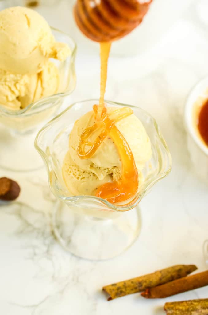 Sundae cups of sexy spices and wildflower honey ice cream being drizzled with honey next to cinnamon sticks