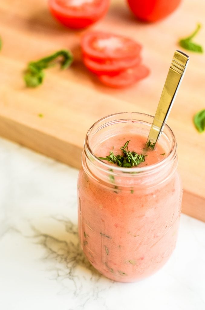 A mason jar filled with tomato basil marinade in front of a cutting board.
