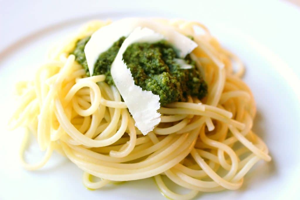 cooked spaghetti topped with pesto and a ribbon of parmesan cheese