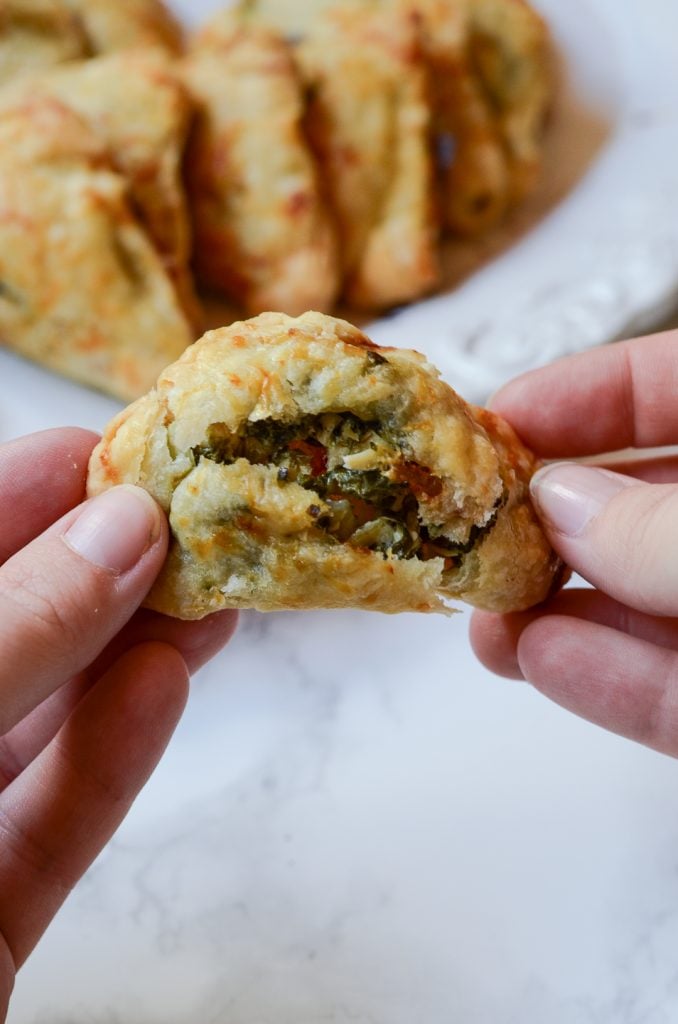 Hands breaking apart a mini hand pie to show bacon, spinach, artichoke, chicken filling