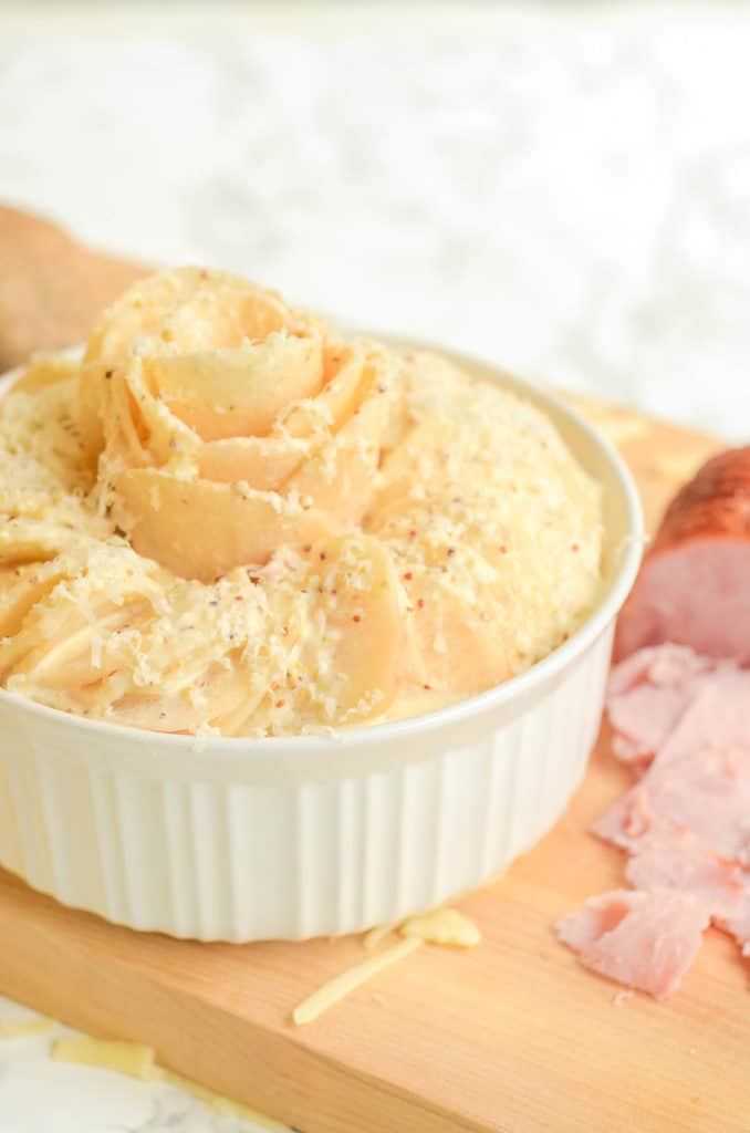 Cut potatoes layered in white corningware on cutting board with sliced ham and cheese