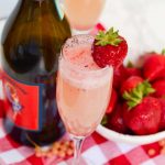 Overhead image of a glass of Bellini with bowl of strawberries and Prosecco bottle