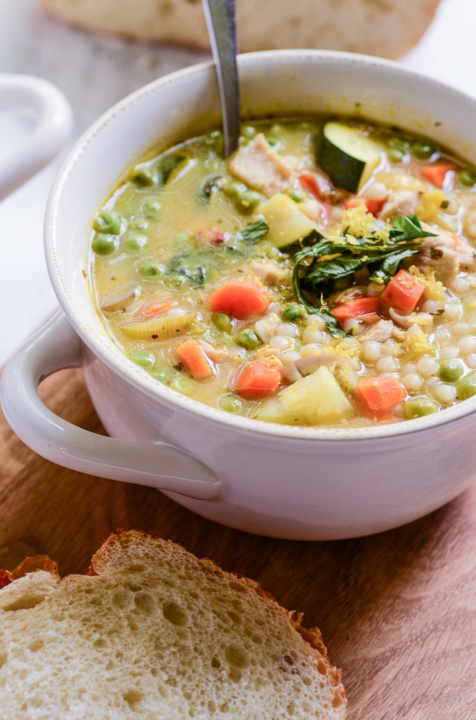 Overhead image of lemony Couscous soup in a white bowl with spoon and bread