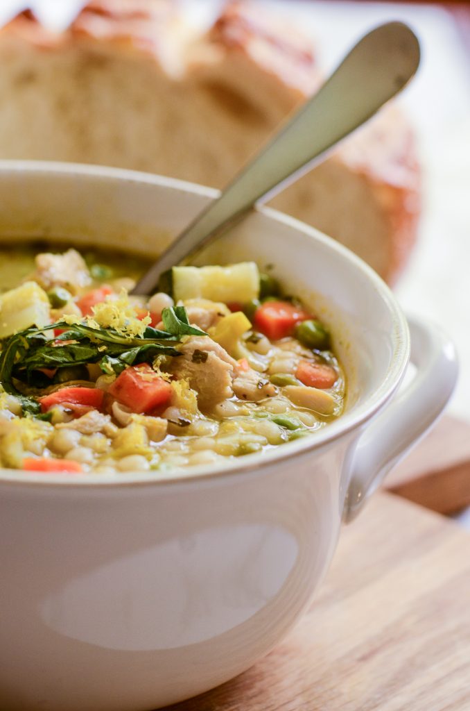 Close up of lemony Couscous soup in a white bowl with spoon and bread