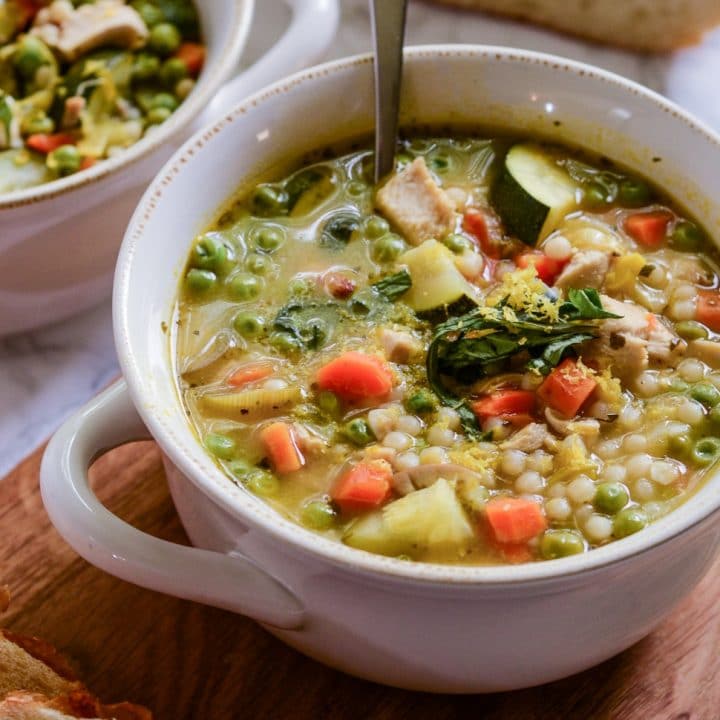 A bowl of couscous soup with a spoon coming out. Crusty bread sits next to it for dipping.