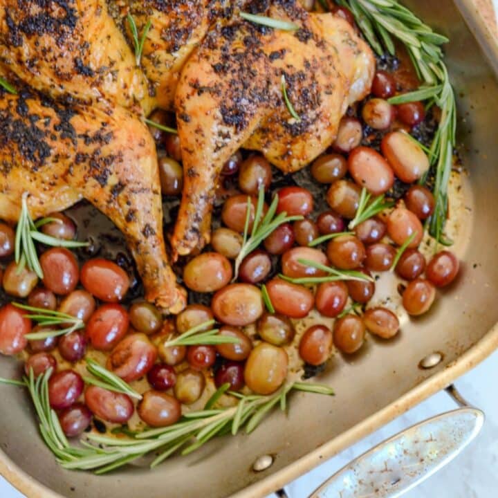 Two pieces of a cooked chicken with tomatoes and rosemary