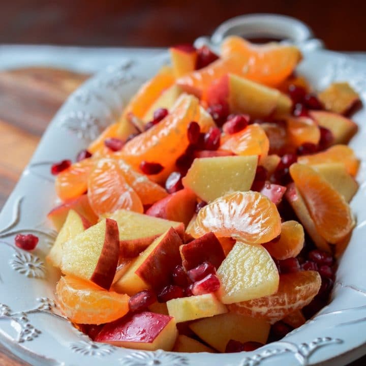 A serving bowl filled with apples, cuties oranges, and pomegranates for winter fruit salad.