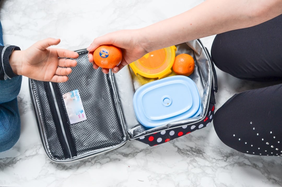 Two hands trading a cutie orange out of a lunch box.