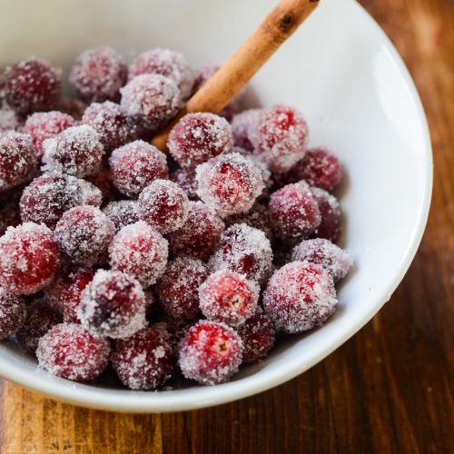 A bowl of sugared cranberries with a cinnamon stick.