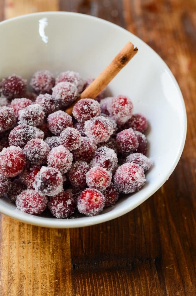 A bowl of sugared cranberries with a cinnamon stick.