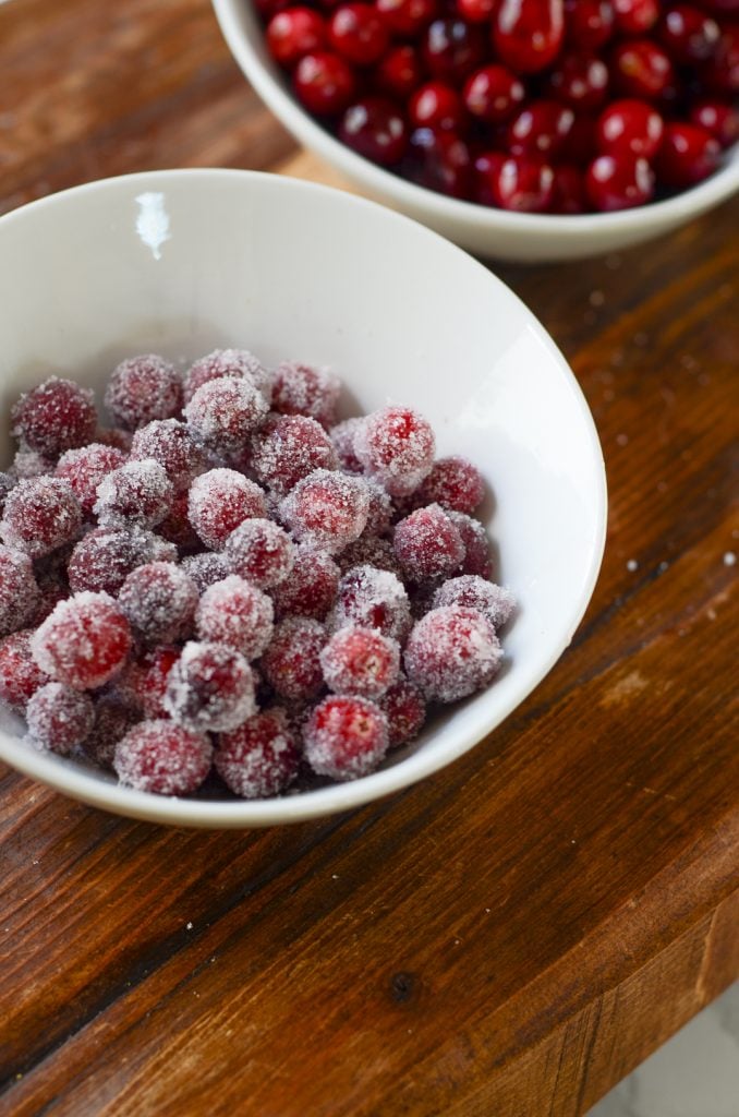 A bowl of sugared cranberries next to a bowl of cranberries